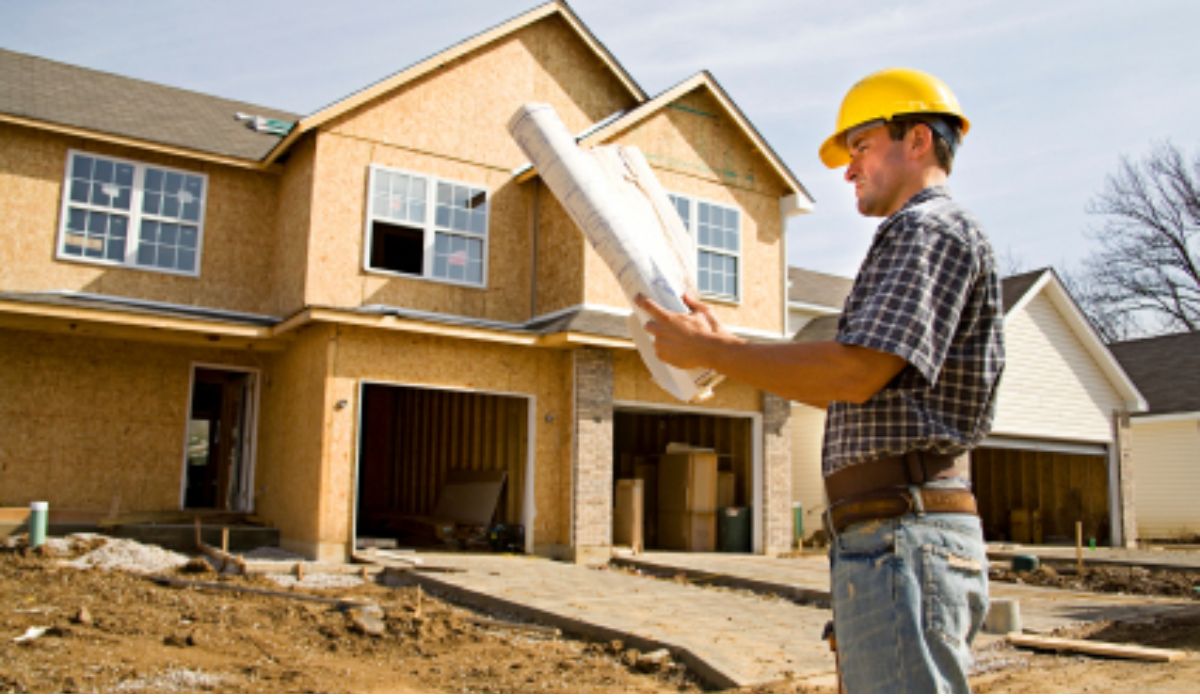 a home building contractor wearing a hard hat and holding a blueprint